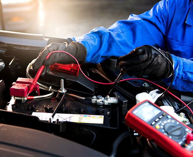 Technician in blue uniform using diagnostic tools on a vehicle battery.