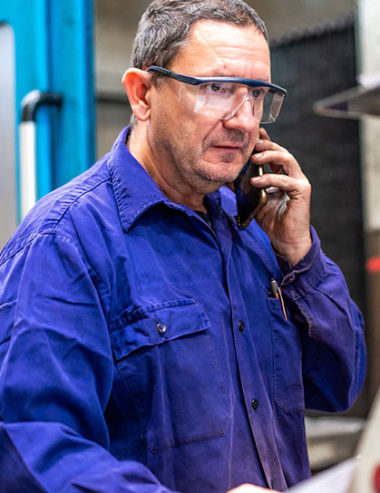 Technician in blue work shirt and safety glasses speaking on the phone.