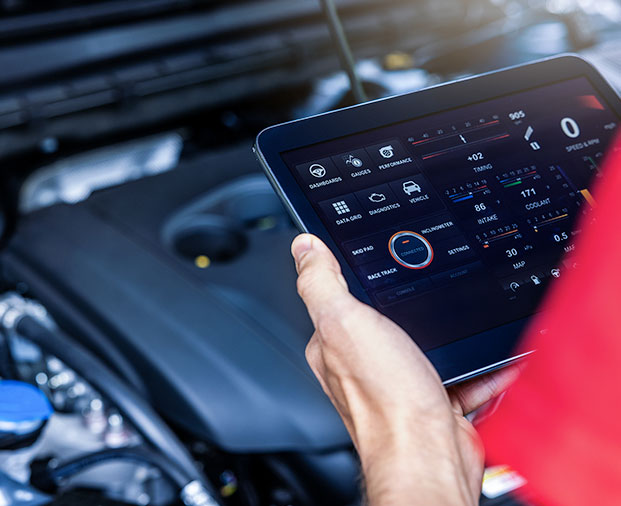 Technician using a tablet with vehicle diagnostics software during engine inspection.