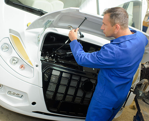 Technician in blue uniform inspecting under the hood of an RV.