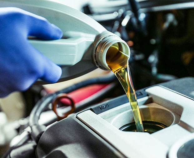 Mechanic pouring motor oil into a vehicle engine during maintenance.