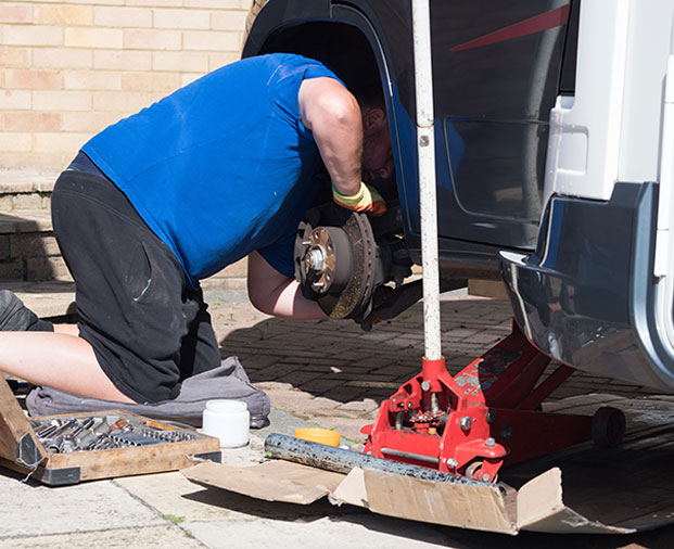 Mechanic kneeling and inspecting a vehicle’s brake system with a wheel removed.