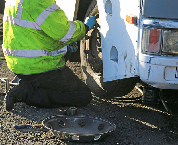 Mechanic in high-visibility jacket repairing a vehicle’s tire on the roadside.