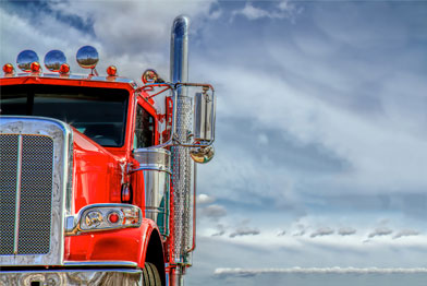 Red semi-truck with chrome details against a cloudy sky.